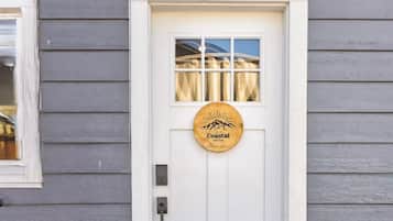 Une porte blanche ornée du logo de Coastal Suites, une fenêtre au-dessus et un banc sur le côté droit.
