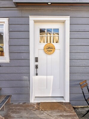 A white door with a Coastal Suites logo, a window above it, and a bench to the right.