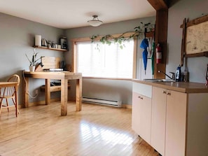 A kitchen with wooden cabinets, a dining table, and a window with blinds. - Coastal Suite – Waterfront Harbour Retreat in the Heart of Ucluelet (Ucluelet)