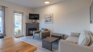 A living room with a fireplace, a television mounted above it, and a sofa. - High Tide - Waterfront Paradise Bachelor (Tofino)