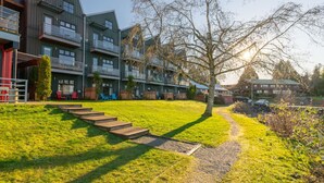 A modern apartment complex with multiple balconies, a grassy lawn, and a clear sky. - High Tide - Waterfront Paradise Bachelor (Tofino)