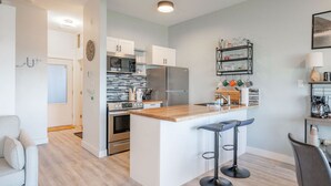 A modern kitchen with a central island, stainless steel appliances, and a bar area with stools. - High Tide - Waterfront Paradise Bachelor (Tofino)