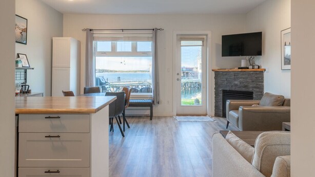 A modern apartment with a kitchen, dining area, and living room. It features a large window with a view of a body of water and a dock. - High Tide - Waterfront Paradise Bachelor (Tofino)
