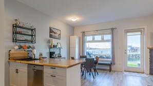 A modern kitchen with a wooden countertop, a dining area with a bench, and a large window offering a view of a dock and water. - High Tide - Waterfront Paradise Bachelor (Tofino)