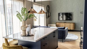 Ein modernes Wohnzimmer mit einer zentralen Kücheninsel, einem Sofa, einem Fernseher und einem Essbereich mit Stühlen.