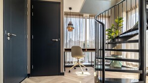 Ein modernes Zimmer mit Holzboden, einem Schreibtisch mit Stuhl, einer Treppe und einem großen Fenster mit Vorhängen.