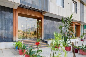 Um edifício moderno com entrada de vidro, plantas em vasos e uma escadaria que leva à entrada.