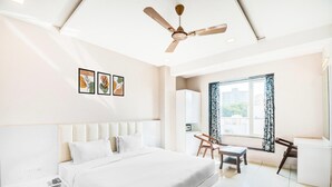 A modern bedroom with a large bed, a ceiling fan, a window with curtains, and a small table. - Comfort and Elegant Stays in Udaipur (Udaipur)