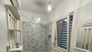 A bathroom with two toilets, a sink, a shower, and a window with blinds.