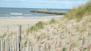 A sandy beach with a rocky outcrop and a wooden fence in the foreground. - Sustainable Stay With Terrace (The Hague)