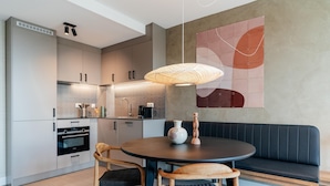 A modern kitchen with a dining area, featuring a round table, two chairs, a bench, and a large abstract wall art piece. - 1 Bedroom Apartment in Den Haag (The Hague)