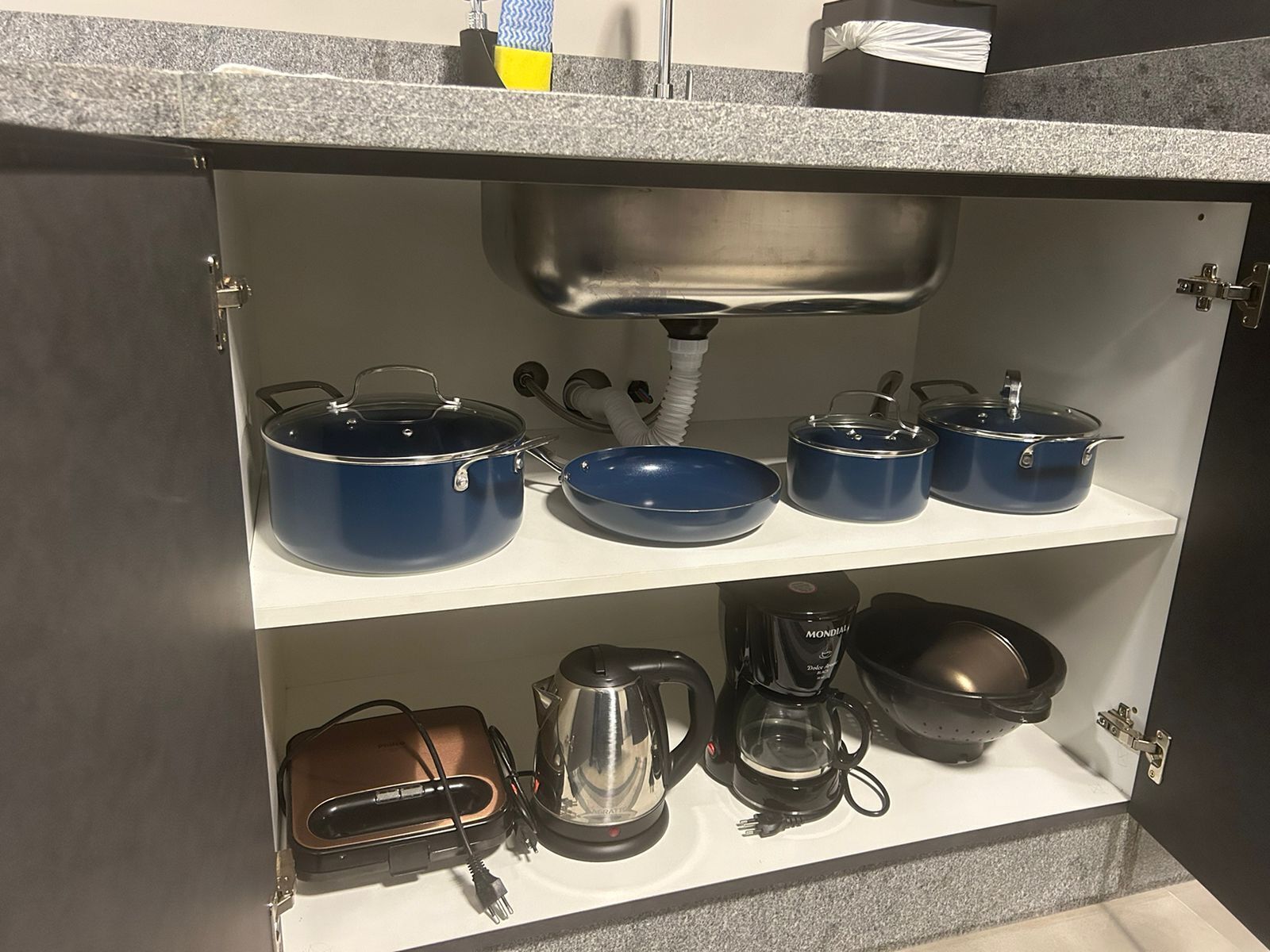 A kitchen with a built-in sink, a coffee maker, a kettle, and various pots and pans on shelves.