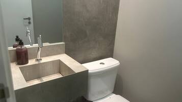 Un bany amb un lavabo beix, un vàter blanc i un mirall sobre el lavabo.