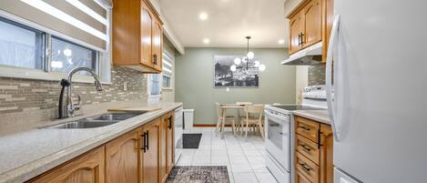 A modern kitchen with wooden cabinets, a granite countertop, a built-in oven, and a refrigerator.