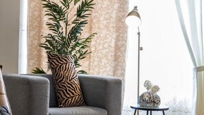 A living room with a grey sofa, a zebra-patterned pillow, a tall floor lamp, a small table with decorative items, and a large potted plant. - Charming Home with Parking & Private Fenced Yard (Mississauga)