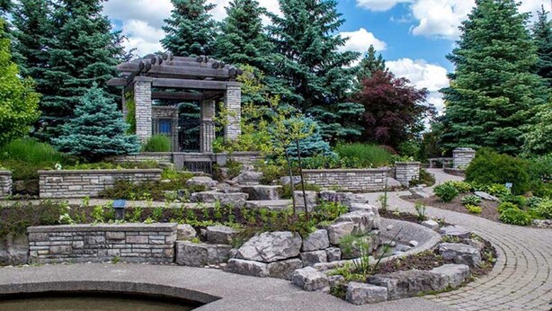 A stone structure with a pergola, surrounded by a landscaped garden with a circular stone feature and a small pond. - Charming Home with Parking & Private Fenced Yard (Mississauga)