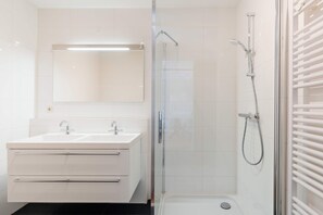A modern bathroom with a glass-enclosed shower, a double sink vanity, and a large mirror. - Comfort Near Scheveningen (The Hague)