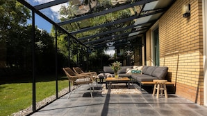 Un patio exterior con cerramiento de vidrio, un sofá, una mesa de centro y sillas de mimbre.