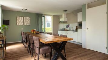 Un comedor con una mesa y sillas de madera, una cocina con armarios blancos y vistas a zonas verdes.