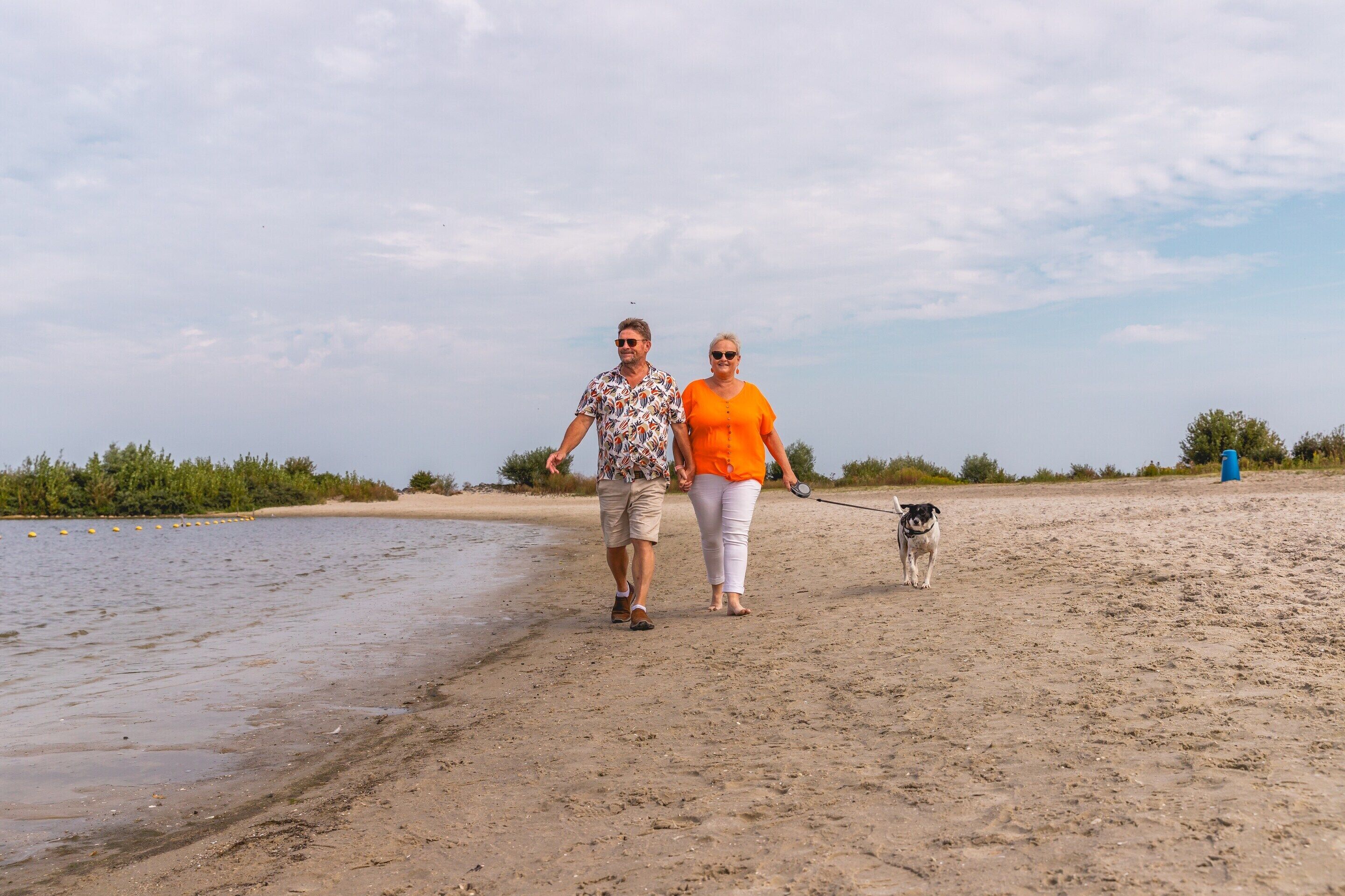 A sandy beach with two people walking a dog.