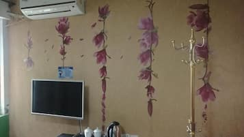 Quarto com ar-condicionado fixado na parede, TV de tela plana, bandeja com chaleira e xícara, e parede decorativa com motivos florais.