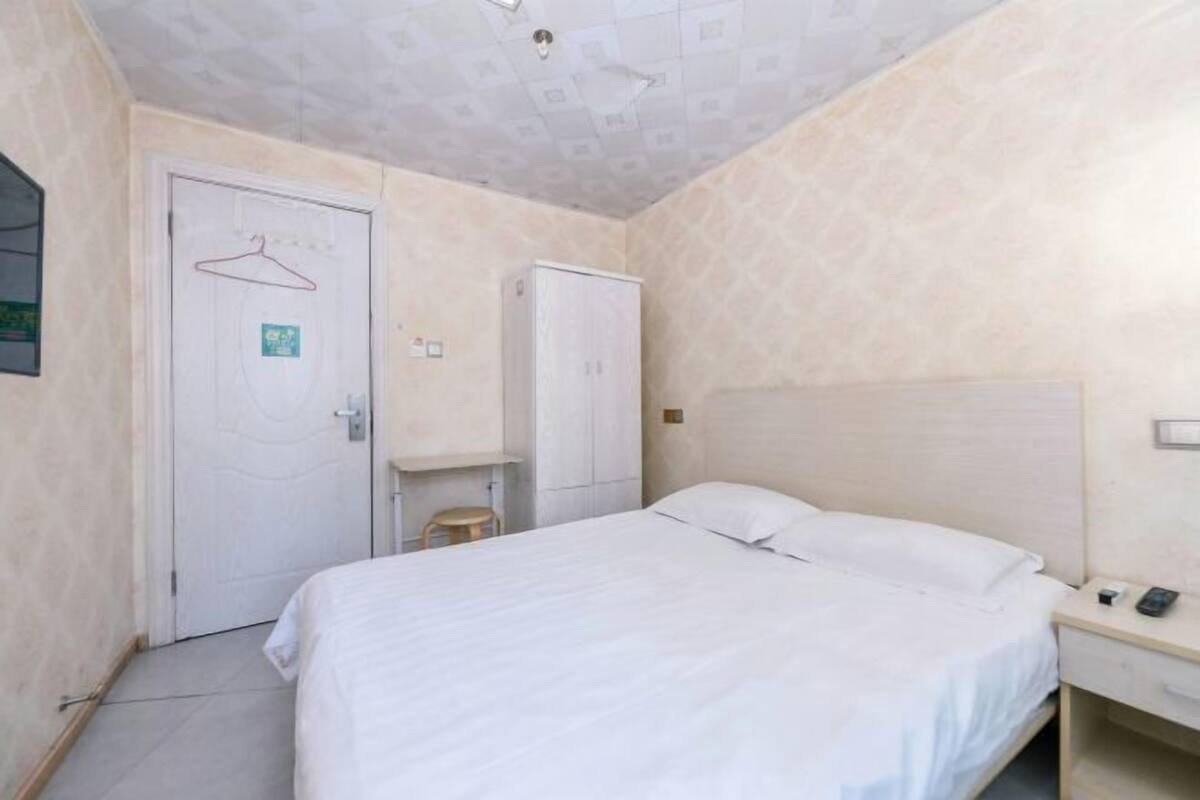 A bedroom with a bed, a wardrobe, a hanging coat rack, and a small stool.