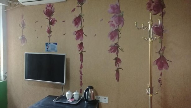 A room with a wall-mounted air conditioner, a flat-screen TV, a tray with a teapot and cup, and a decorative wall with floral patterns. - Changlai Hostel (Shanghai)
