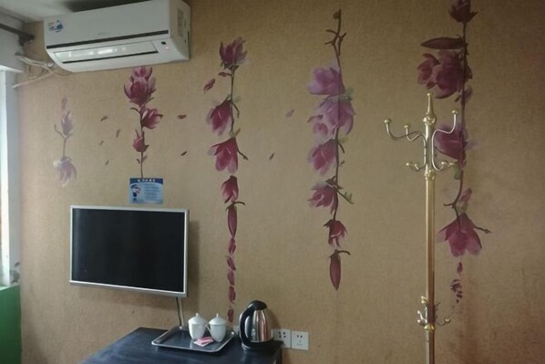 A room with a wall-mounted air conditioner, a flat-screen TV, a tray with a teapot and cup, and a decorative wall with floral patterns. - Changlai Hostel (Shanghai)