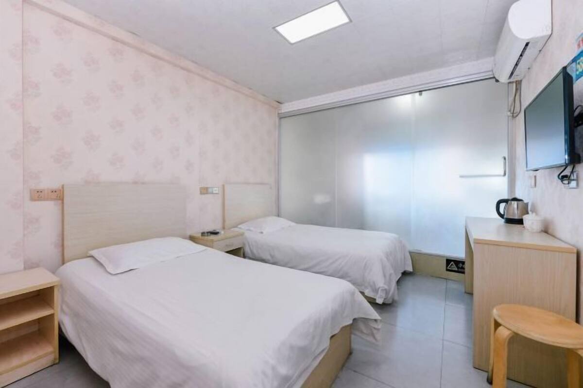 A hotel room with two single beds, a desk with a chair, a TV, and a wardrobe.