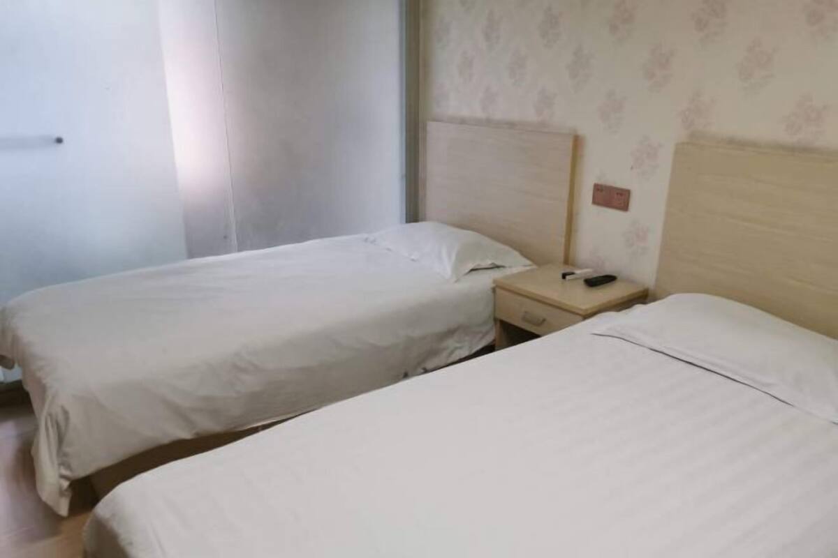 A room with two beds, a nightstand with a phone, and a wall with floral wallpaper.