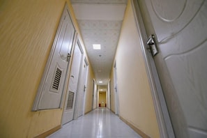 A long, narrow hallway with doors on both sides, a light fixture on the right wall, and a ceiling light at the end. - Changlai Hostel (Shanghai)