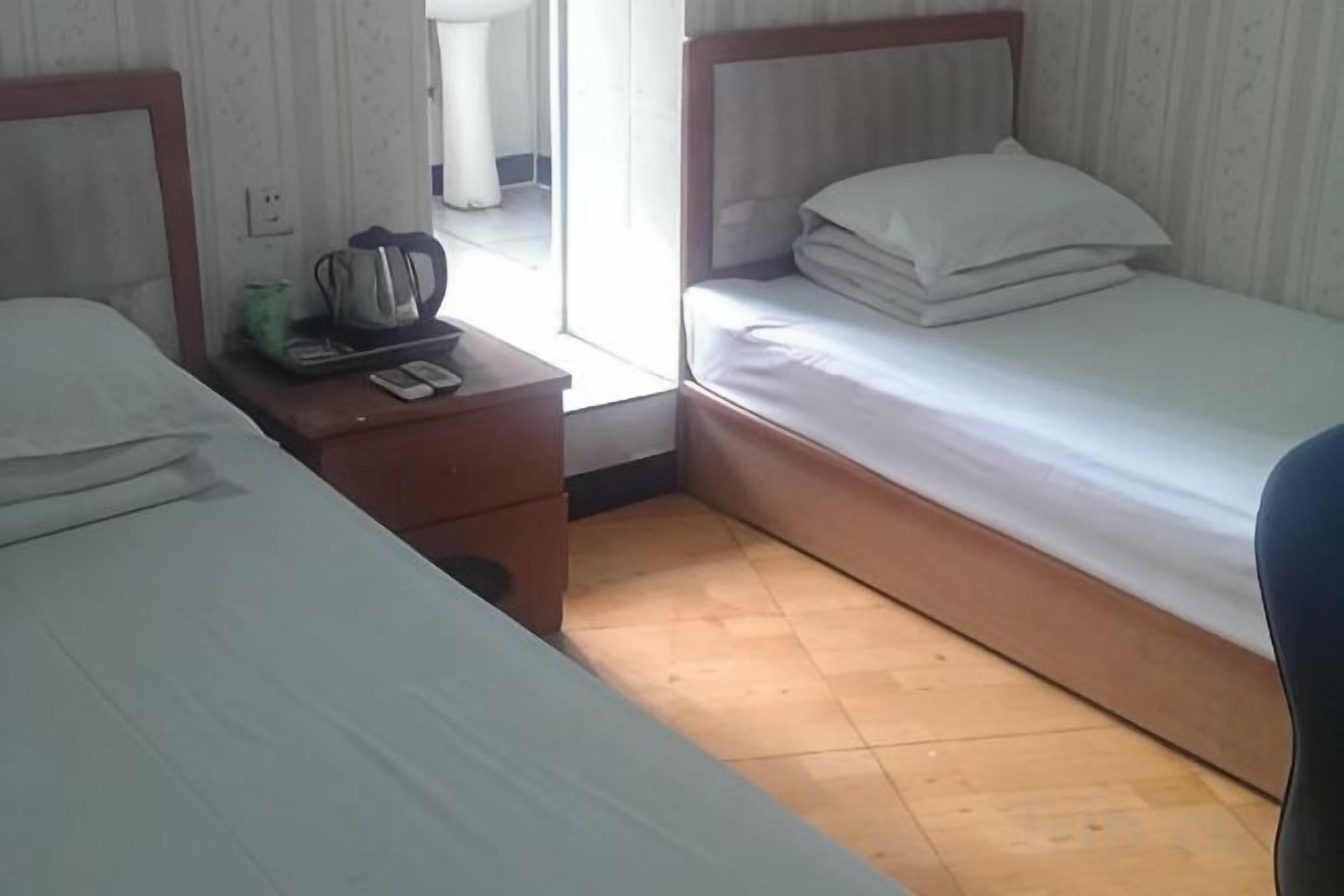 Quarto de hotel com duas camas, uma mesa de cabeceira de madeira, uma mesinha e uma cadeira.