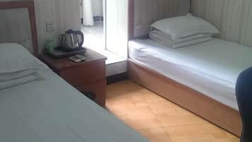 Quarto de hotel com duas camas, uma mesa de cabeceira de madeira, uma mesinha e uma cadeira.