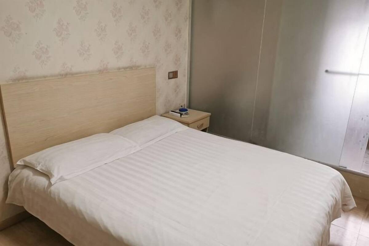 A bed with a wooden headboard, a nightstand with a book and a lamp, and a patterned wallpaper on the wall.