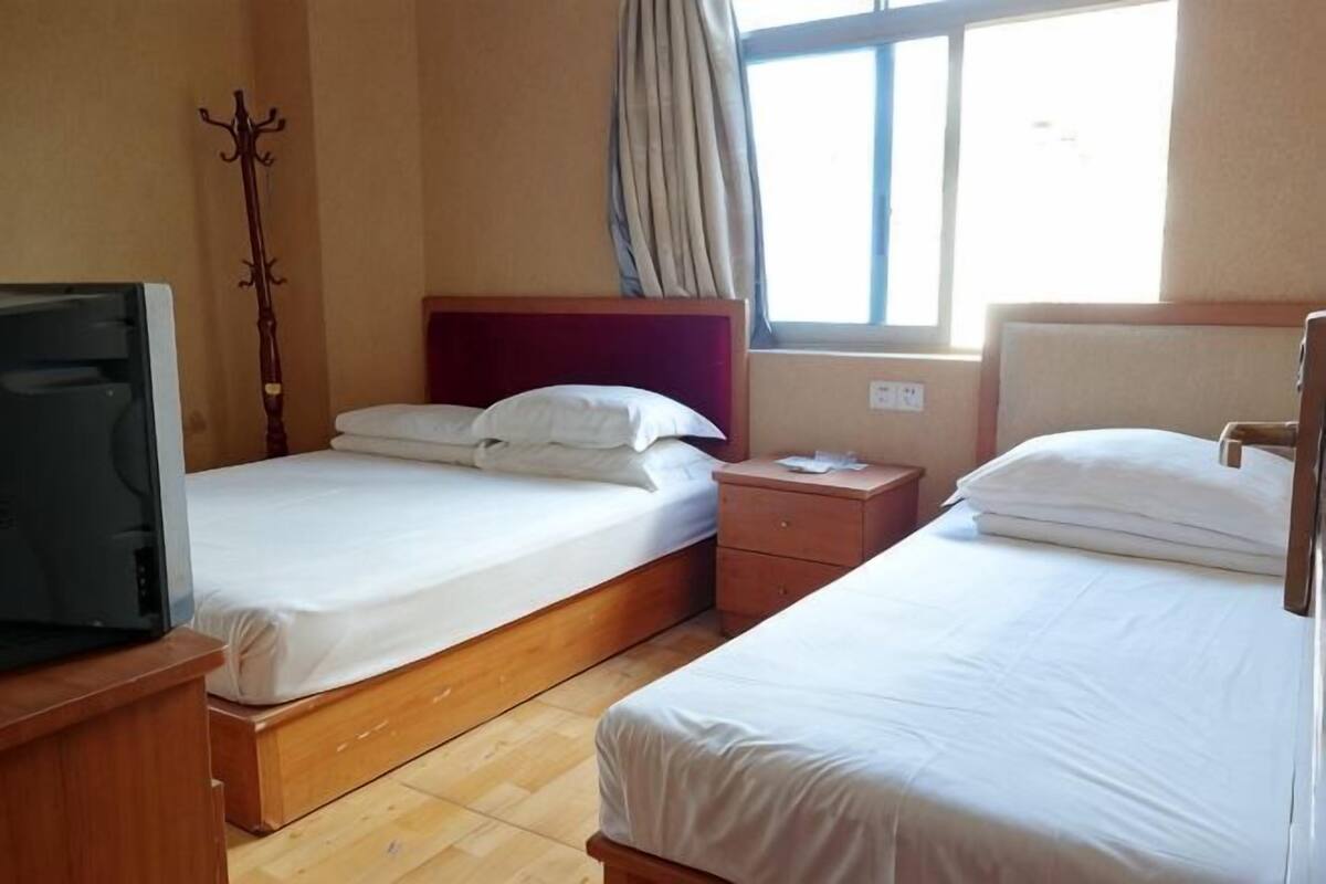 A hotel room with two beds, a TV, a window with curtains, and a wooden floor.