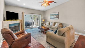 A living room with a fireplace, a ceiling fan, a sofa, a coffee table, and a TV. - Beach House - Hooked on the Cape by PHG (Port St. Joe)