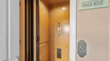 Un ascensor con un cartel que dice 'BEACH HOUSE' y un panel de control con botones.