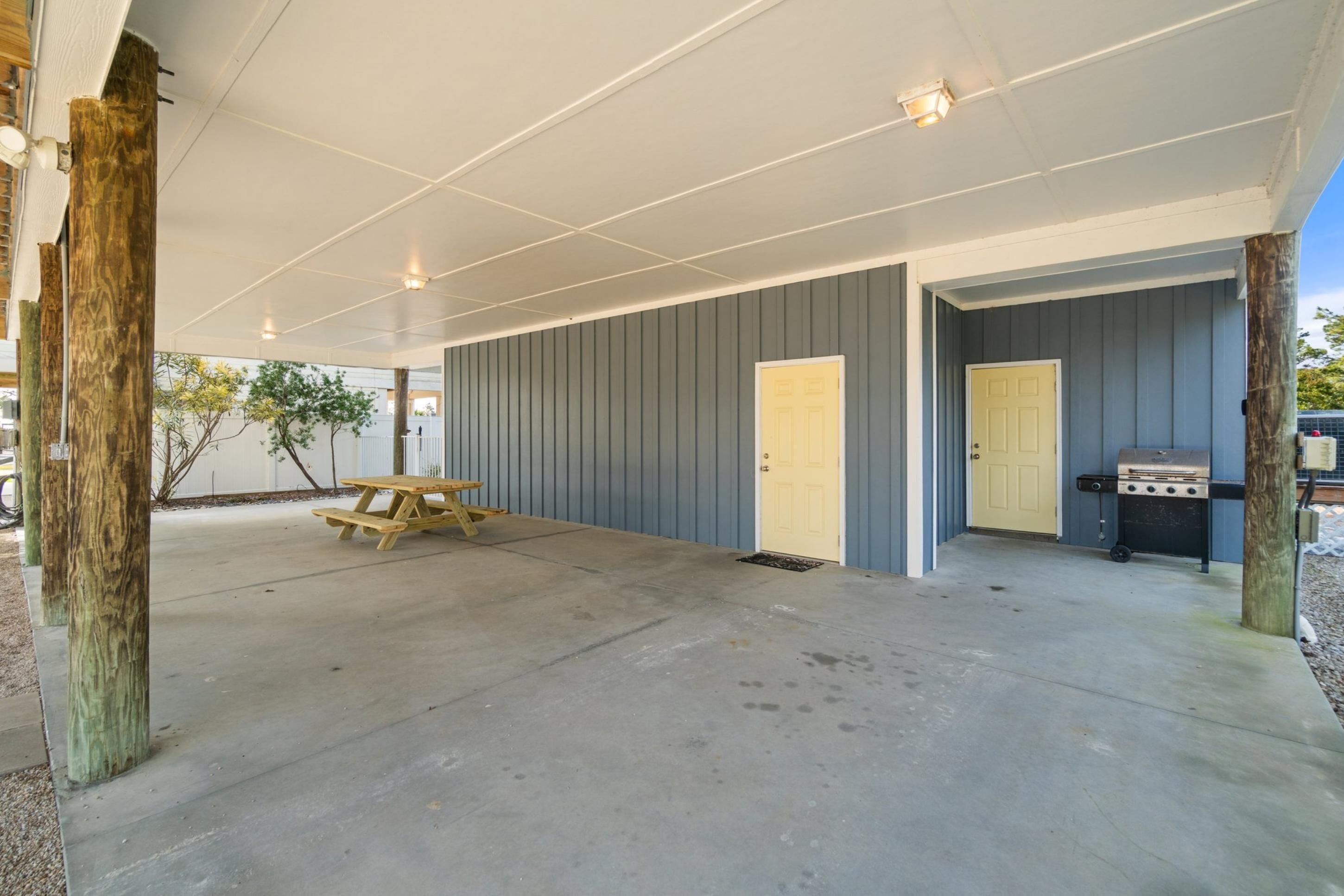 An outdoor covered patio area with a picnic table, a grill, and two doors.