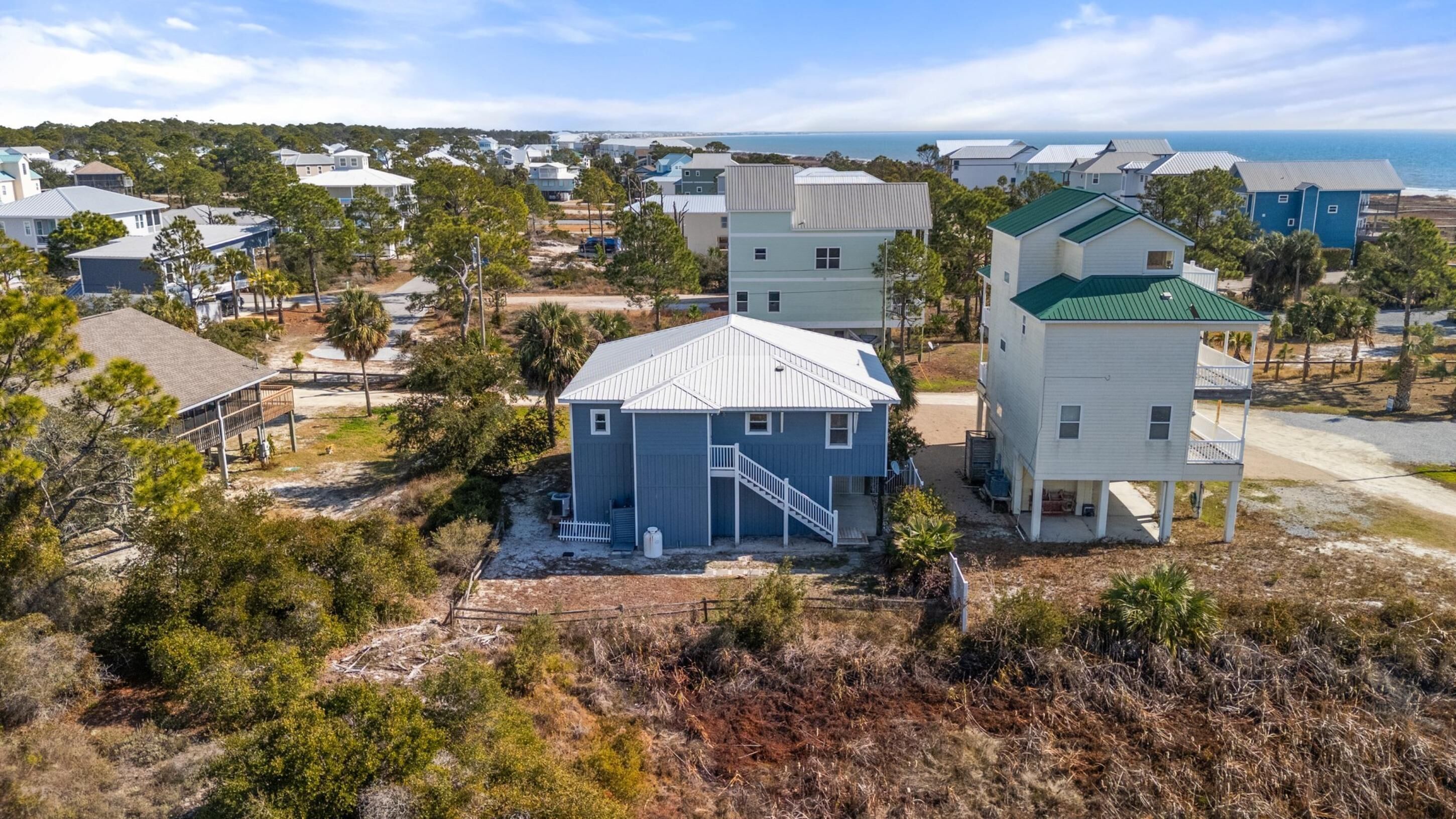Et kystnært boligområde med huse i forskellige arkitektoniske stilarter, herunder et markant hus med blåt tag og et hvidt hus med grønt tag.