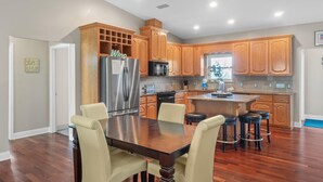 A kitchen with wooden cabinets, a stainless steel refrigerator, a microwave, and a dining area with a wooden table and chairs. - Beach House - Hooked on the Cape by PHG (Port St. Joe)