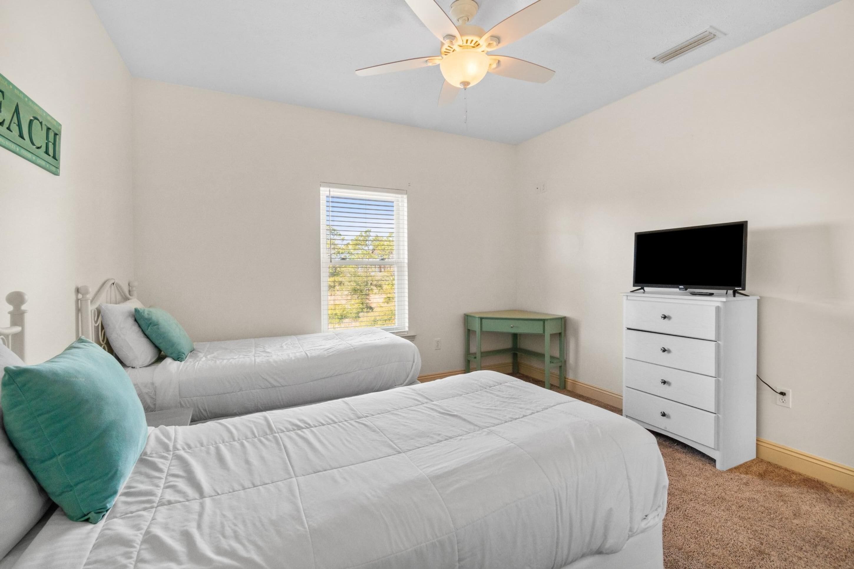 Une chambre avec deux lits, un ventilateur de plafond, une fenêtre, un téléviseur et une commode.