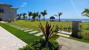 A well-maintained lawn with a stone pathway leading to a building, palm trees, and a clear view of the ocean.