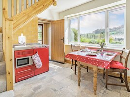 Una cocina con estufa roja, una escalera de madera y un comedor con mesa lista para dos personas.