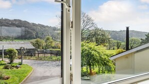 A window with a view of a rural landscape, including a road, a fence, and a building. - Pant Y Cwtsh (Kidwelly)