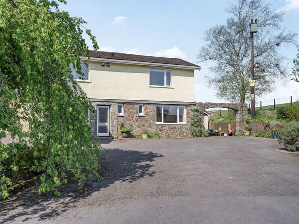 A two-story house with a stone facade, a front door, and a driveway leading to a stone archway. - Pant Y Cwtsh (Kidwelly)