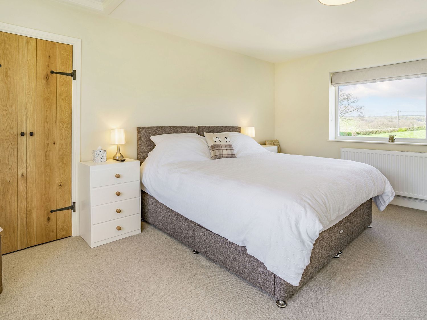A bedroom with a large bed, bedside tables, a wardrobe, and a window with a view.