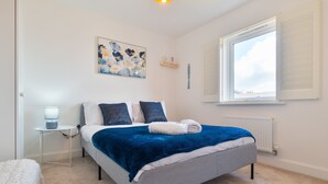Une chambre à coucher comprenant un lit, une table de chevet, une lampe, un radiateur et une fenêtre avec des stores.