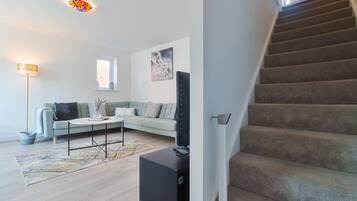 A modern living room with a sofa, coffee table, and a flat-screen TV. A staircase is visible to the right.