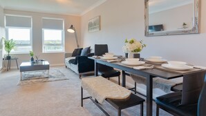 Un comedor moderno con una mesa larga preparada para cuatro personas, un banco y un sofá al fondo.