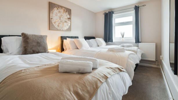 Habitación de hotel con dos camas, un ventanal con cortinas, un radiador y una obra de arte colgada en la pared.